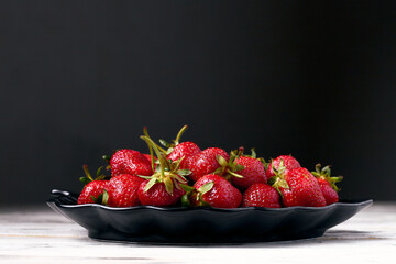 Fresh strawberries in black plate on white wooden table