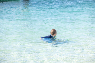 Boy swimming in translucent blue water at the beach on holiday