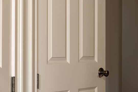 Partially open white wood six panel door with a shallow depth of field background with copy space