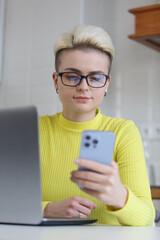 Beautiful white woman with short dyed hair networking with clients online. Stylish young female using modern blue smart phone