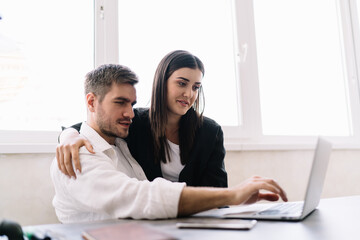 Cheerful couple working on laptop in office