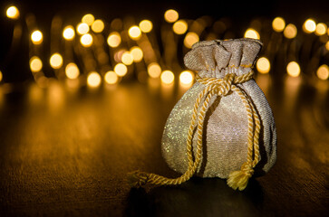 Small golden gift bag on a black background illuminated by light from side, round yellow blurred lights behind