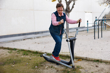 Fototapeta na wymiar An elderly woman is engaged in sports on street simulators, Physical education in retirement