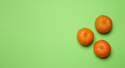 Three ripe mandarins on green background, top view. Ripe fruit