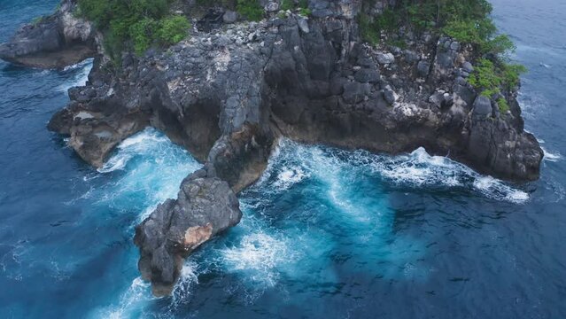 Beautiful static aerial footage of ocean waves and rip current around rocky island. Drone shot of blue sea maelstrom. Swirl of turquoise water around reef and high cliffs. Blue foam splashing on stone