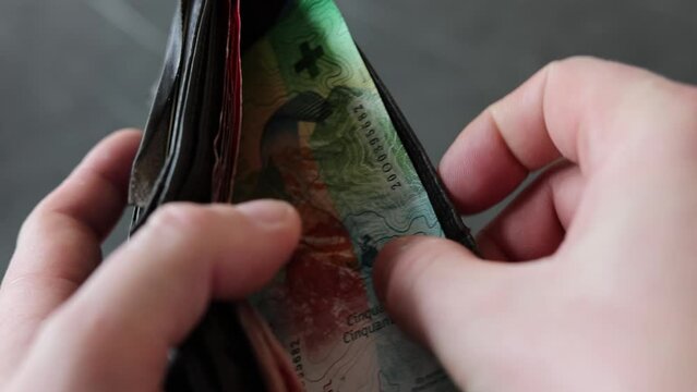 A man looks for money in his wallet and pulls out 50 Swiss francs.