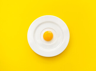 White plate with chicken yolk on yellow background. Concept of foods rich in vitamin D or ingredient for baking. Close-up