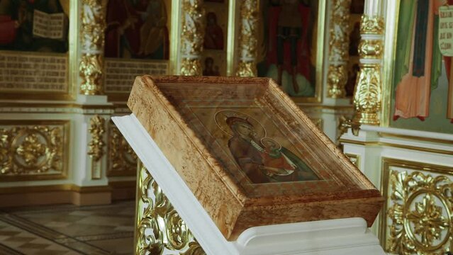 Icon of the Mother of God with the baby under glass lies on white pedestal in the church. Golden interior of the temple.