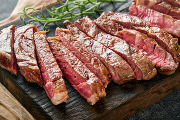 Steaks. Sliced grilled meat steak New York or Ribeye with spices rosemary and pepper on black marble board on old wooden background. Top view. Mock up.