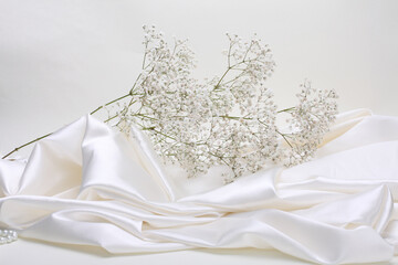 Beige pearl wave fabric silk and Gypsophila flower twig. Abstract texture horizontal copy space...