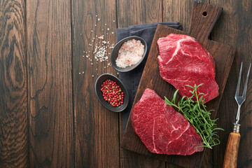Raw beef steak. Marbled raw fresh Ribeye steak with rosemary, salt and pepper on cutting board on dark concrete background. Raw beef steak and spices for cooking.