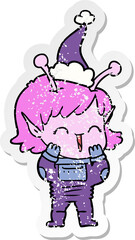 distressed sticker cartoon of a alien girl giggling wearing santa hat