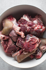 Fresh raw goat meat in a white bowl, chopped goat meat being prepared for cooking