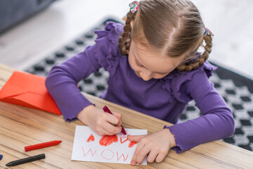 cute little girl is drawing a greeting card for her mother with red heath shape . Happy Mother's Day or womans day concept 