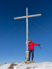 Hiker on top of peak with summit cross with snow landscape background