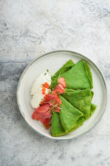Green pancakes. Round thin green spinach crepe pancakes with red and black caviar and yogurt sauce on gray concrete background. Healthy vegan breakfast. National Pancake Day or Fat Tuesday Day.