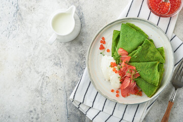 Green pancakes. Round thin green spinach crepe pancakes with red and black caviar and yogurt sauce on gray concrete background. Healthy vegan breakfast. National Pancake Day or Fat Tuesday Day.