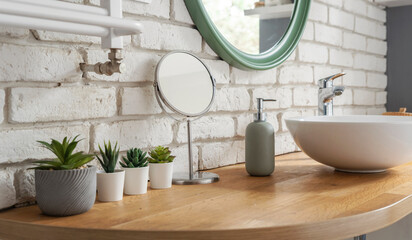 Bathroom in modern style with wooden counter, ceramic wash basin, round mirror, brick wall and...