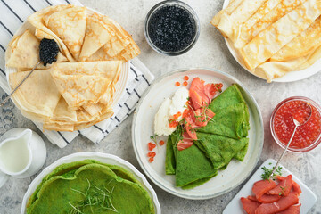 Green and white pancakes assorted. Thin green spinach and white crepe pancakes with red and black caviar, sauce on gray concrete table background breakfast. National Pancake Day or Fat Tuesday Day.