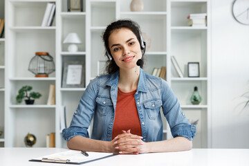 Young curly brunette woman wearing video call headset on laptop in home light office. Video conference, remote meeting. Programmer, remote work, work from home.