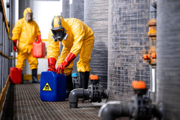 Fully protected workers in yellow hazmat suit, gas masks and gloves handling biohazardous chemicals...