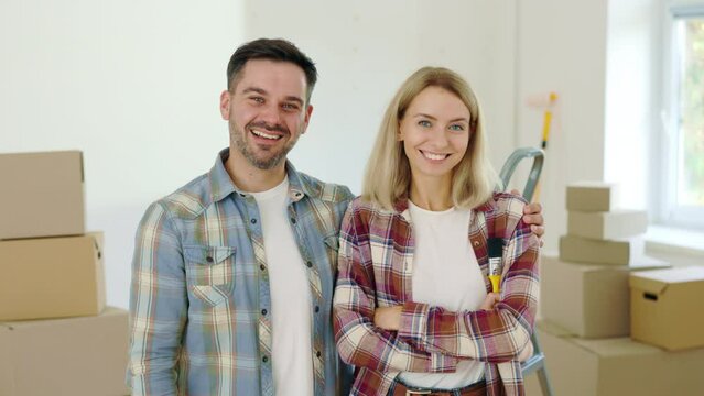 Portrait of the Happy Couple Who Makes Repairs in a New House. Smiling Family Standing in Their Apartment with Paint Brush in Hand. Relocation, Moving and Repair Concept