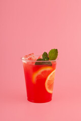 Red Fruit Sangria in disposable take away cup on pink background. Summer refreshing drink. Iced cocktail with natural juice and leaf mint