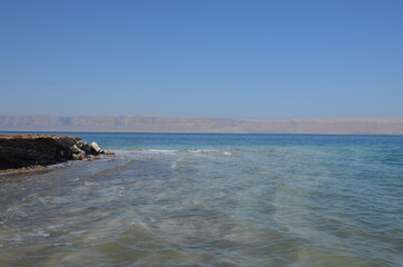 Fototapeta na wymiar Panoramic view of the beautiful, clear blue Dead Sea shimmering and shining on a bright sunny day in Jordan and the dry land around it.