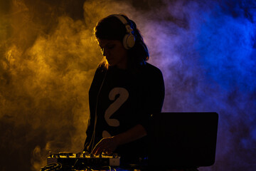 Silhouette female DJ on a mixer. Girl playing texhno music against smoke background.