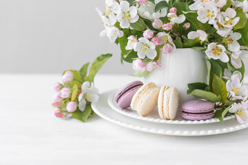 Obraz na płótnie Canvas Beautiful composition with delicious French macarons and spring flowers in a white cup. Sweet dessert, early spring white and pink flowers, wedding decor, bride morning