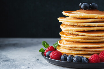Delicious pancakes, with fresh blueberries, raspberry and maple syrup or honey on a dark background