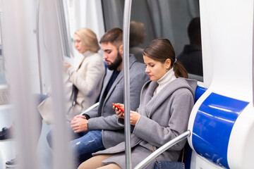 Young focused woman browsing and typing messages on phone on way to work in modern metro car