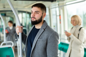 Fototapeta na wymiar Young bearded man in light overcoat riding in modern streetcar. Concept of daily city commuting