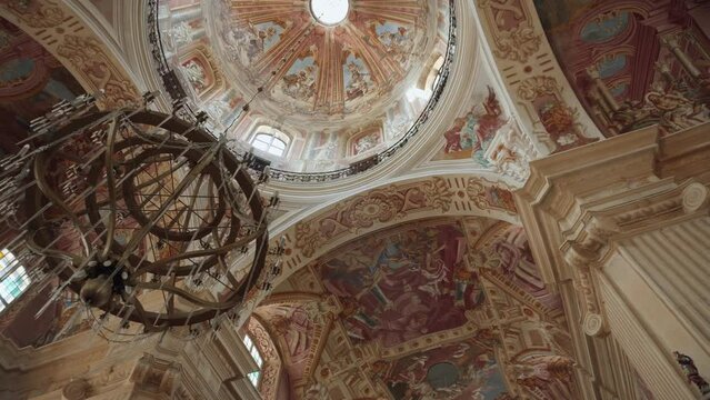 Up view of ceiling and dome old Farny Church in Nesvizh, rich decorated frescoes. Baroque chandelier hangs from highest point building. Temple built in 16th century.