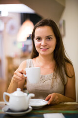 Portrait of glad young girl rests in cafe behind cup of tea