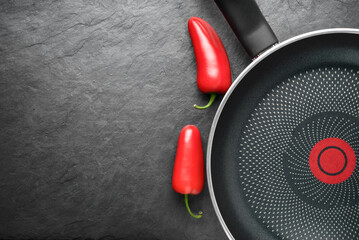 Blank skillet with non-stick coated surface on the black slate with red peppers. Copy space.