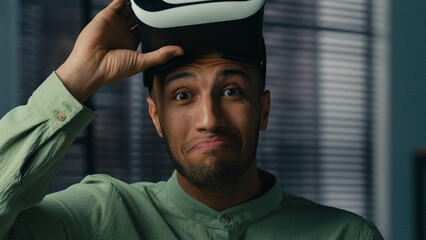 Surprised african american man take off VR glasses in 3D metaverse world play online male gamer...