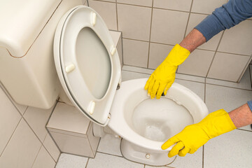 Hands of a man in yellow gloves cleaning the toilet bowl in the bathroom