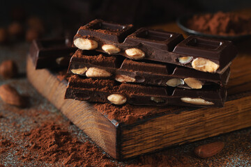 Dark and milk chocolate with nuts on a dark background sprinkled with cocoa powder.