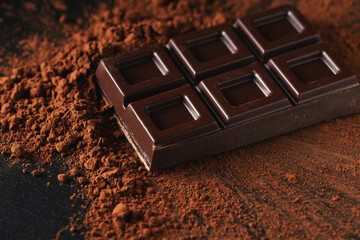 Dark and milk chocolate with nuts on a dark background sprinkled with cocoa powder.