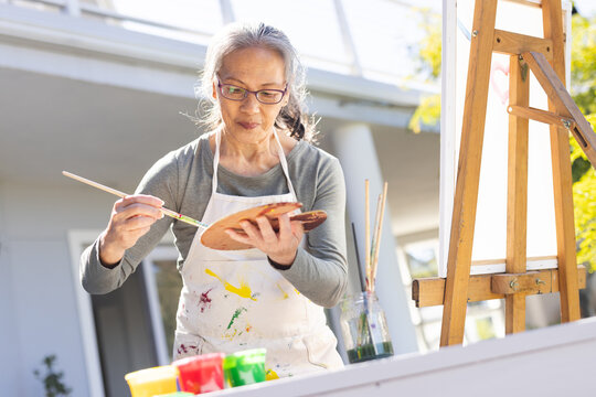 Fototapeta Happy senior asian woman painting on easel in garden