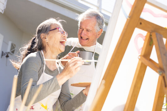 Happy senior diverse couple painting on easel in garden