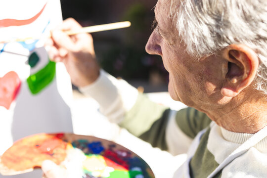 Happy senior caucasian man painting on easel in garden