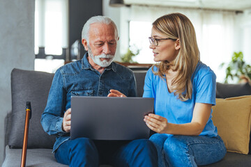 Nurse help senior man with internet and laptop on the sofa in a retirement home. Healthcare worker,...
