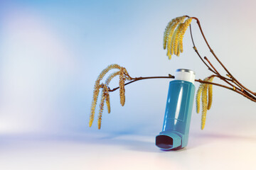 Inhaler with allergy spray in front of hazel branches with catkins and pollen which can cause...