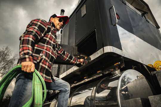 Semi Truck Driver Preparing Trailer Cargo Straps Next to His Tractor