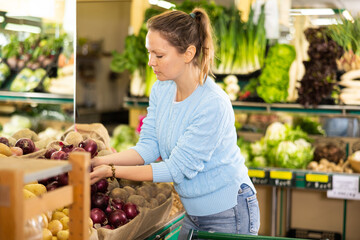 Smiling middle-aged woman customer buying red onions at the counter in big greengrocery