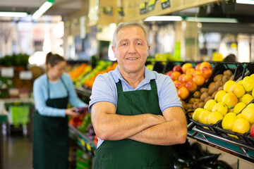 Portrait of skilled male seller in uniform looking at camera during work day in grocery supermarket