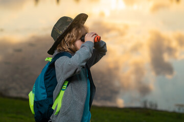 Young boy looking through binoculars. Imagination or exploration in park. Happy child playing with binocular. Young tourist explorer. Child vacation and travel. Summer journey for kids.