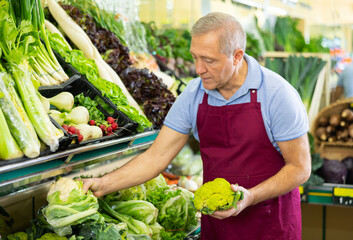 male seller of vegetable shop chooses fresh and ripe cauliflower for regular customer